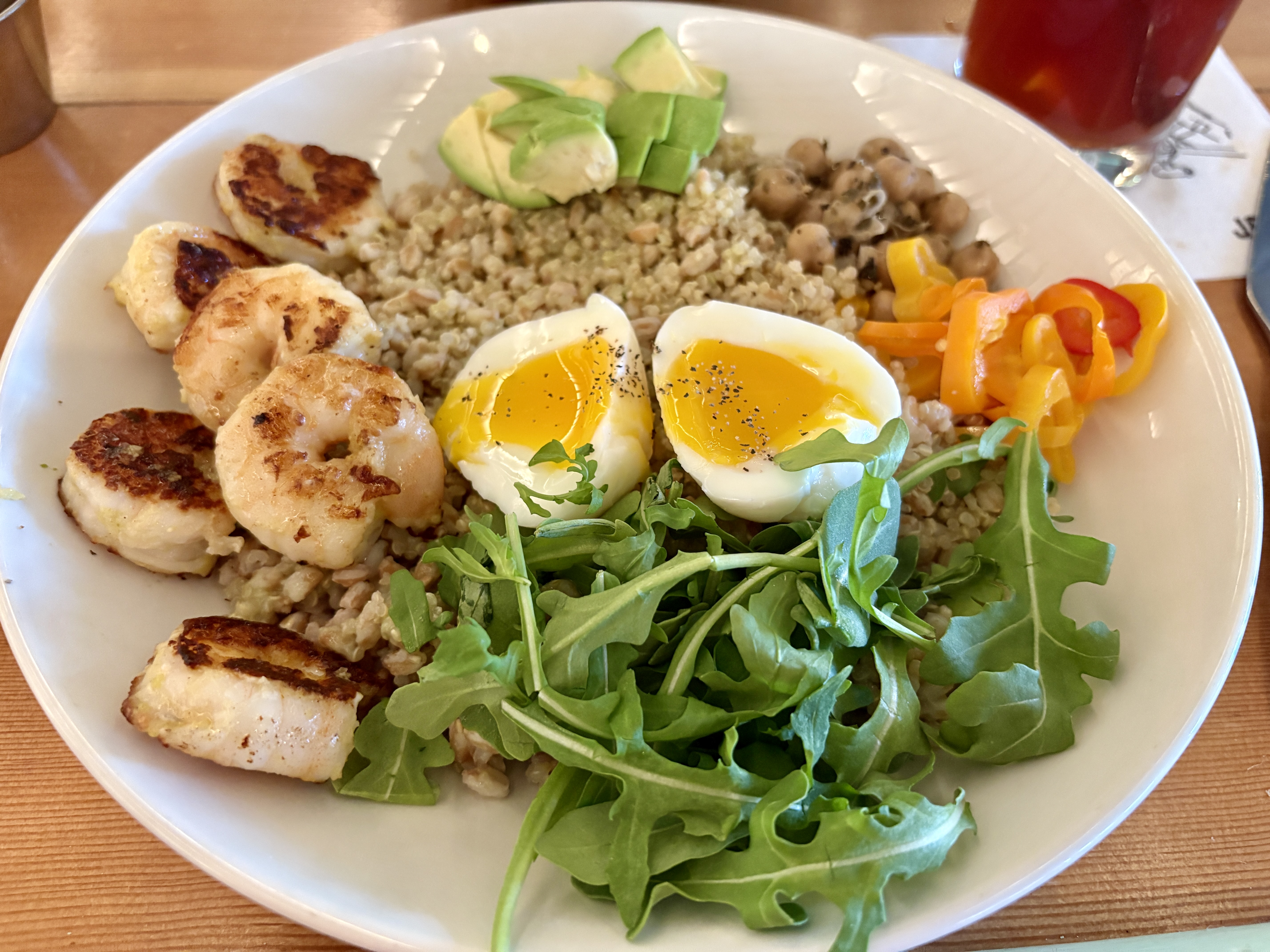 A white bowl holds grains, grilled shrimp, arugula, a soft boiled egg, and chickpeas.