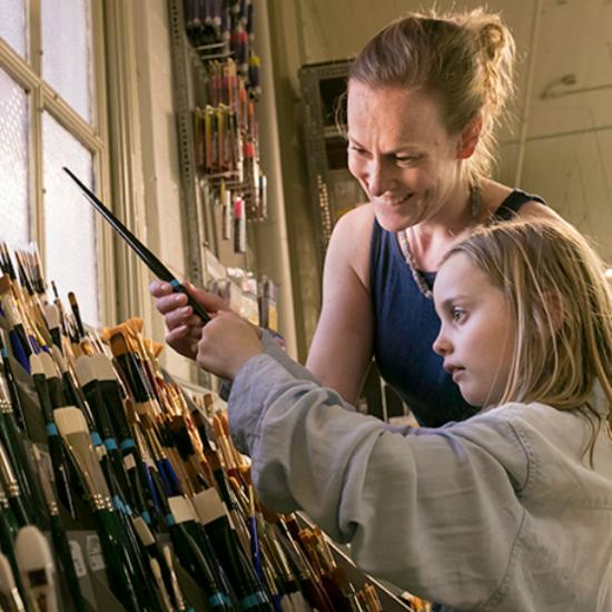 An adult and child happily looking together at a large rack of paint brushes