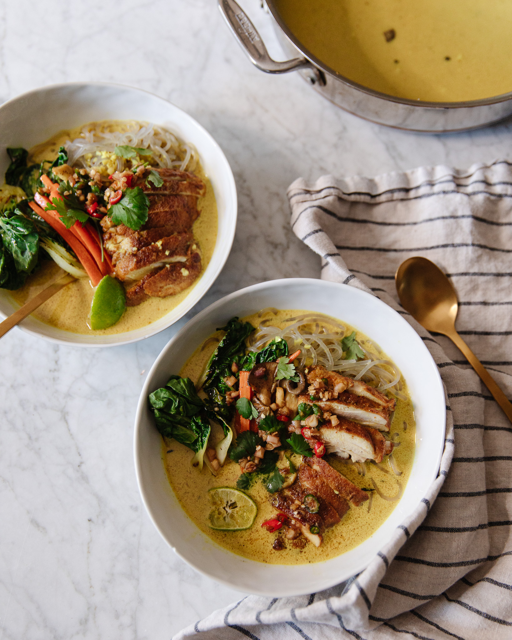 Two bowls of coconut curry soup with glass noodles and chicken on a marble countertop