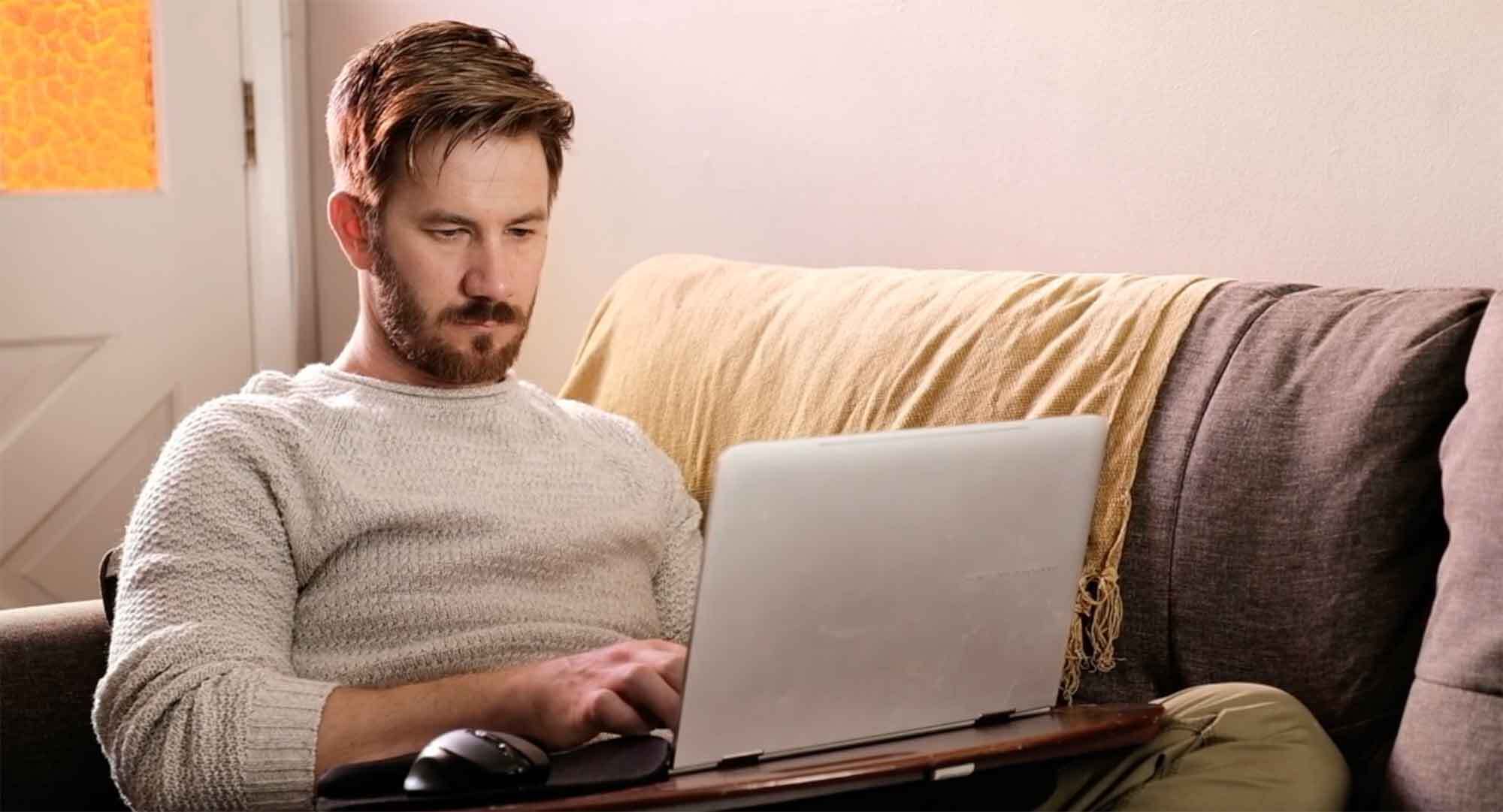 A man sitting on a couch using a laptop, with a focused expression.