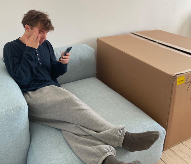 Une photo d'un homme assis sur un canapé qui regarde son téléphone tout en se tenant la tête.