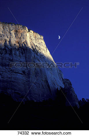 Stock Photo of Mountain cliff with deep blue sky and quarter moon.