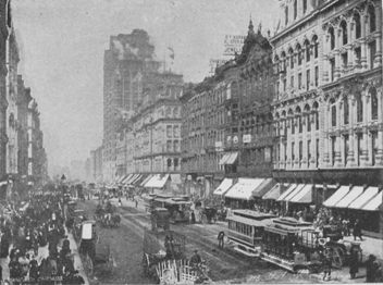 Busy city street flanked by tall buildings with shops on the bottom floors.