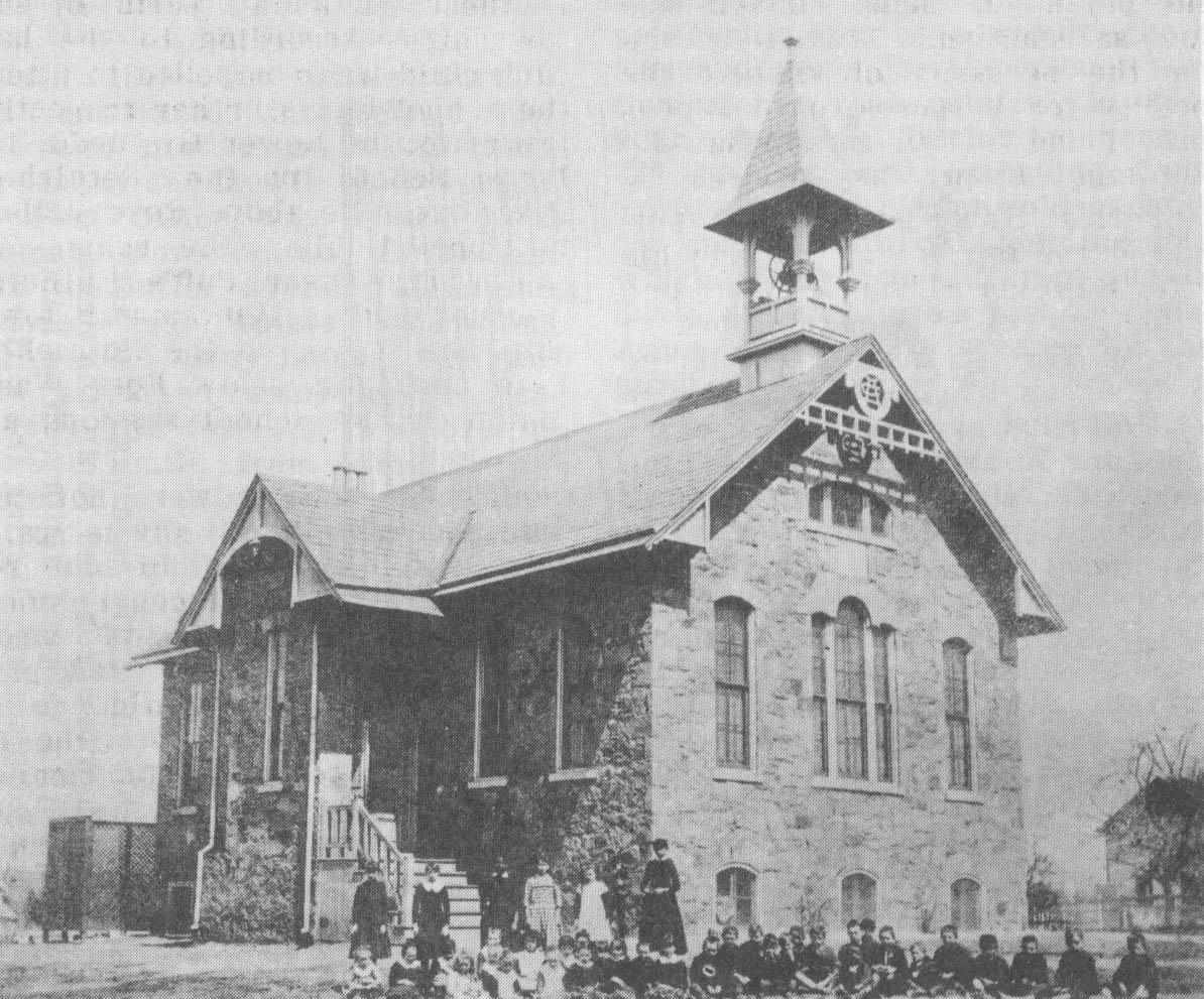 Photograph of the school with students and teachers outside.