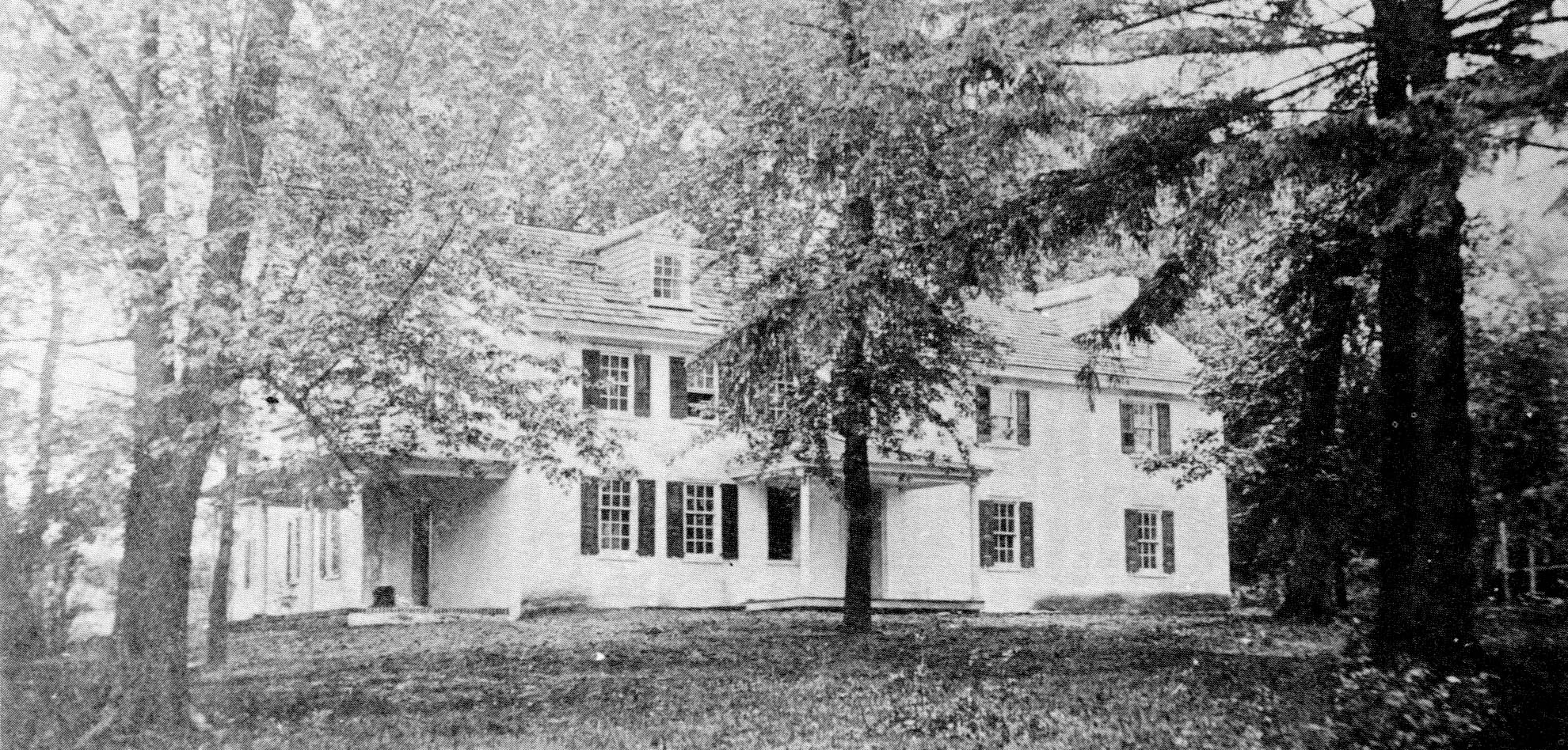 Large white house surrounded by a yard with many trees.