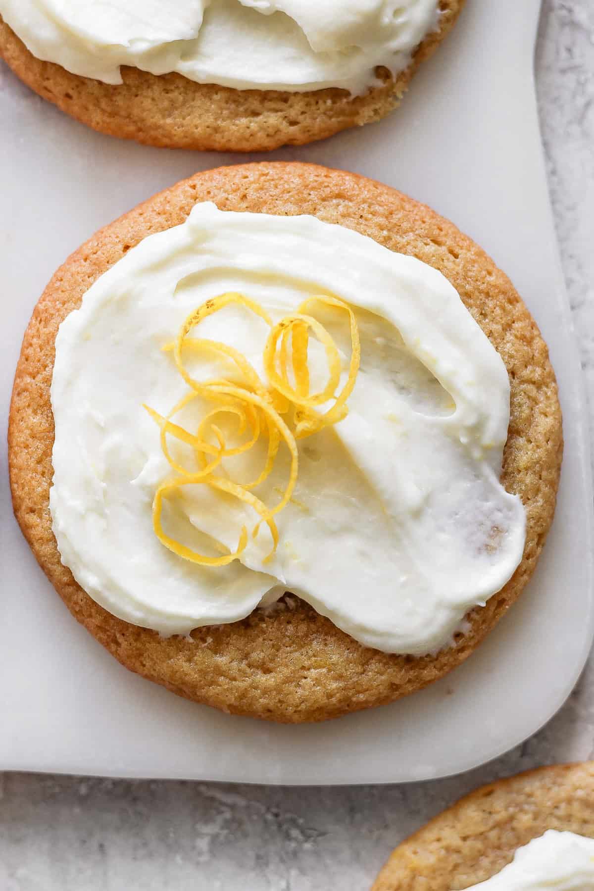 A lemon cookie adorned with cream cheese frosting and garnished with a twist of lemon peel.