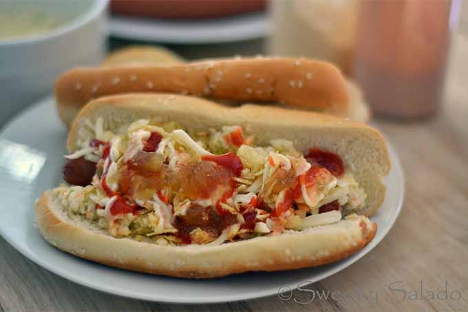 Colombian Hot Dogs with chopped vegetable and sauce, on a white ceramic plate.