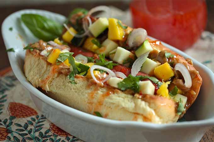 Thai Peanut Hot Dogs with chopped vegetables on top, in a white oblong dish.