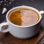 Bone Broth in a two-handled mug on a cutting board