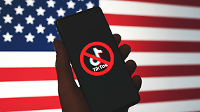 A hand holding a smartphone displaying a 'No TikTok' symbol against a US flag background.