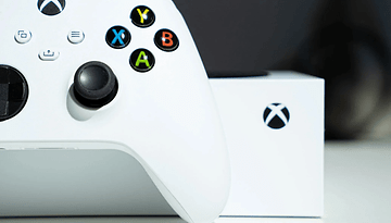 An Xbox controller in white with colorful buttons next to an Xbox box.