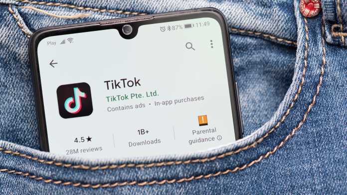 Aus der Hosentasche einer Jeans lugt ein Handy hervor. Auf dem Bildschirm ist ein App-Store mit Tiktok-App zu sehen