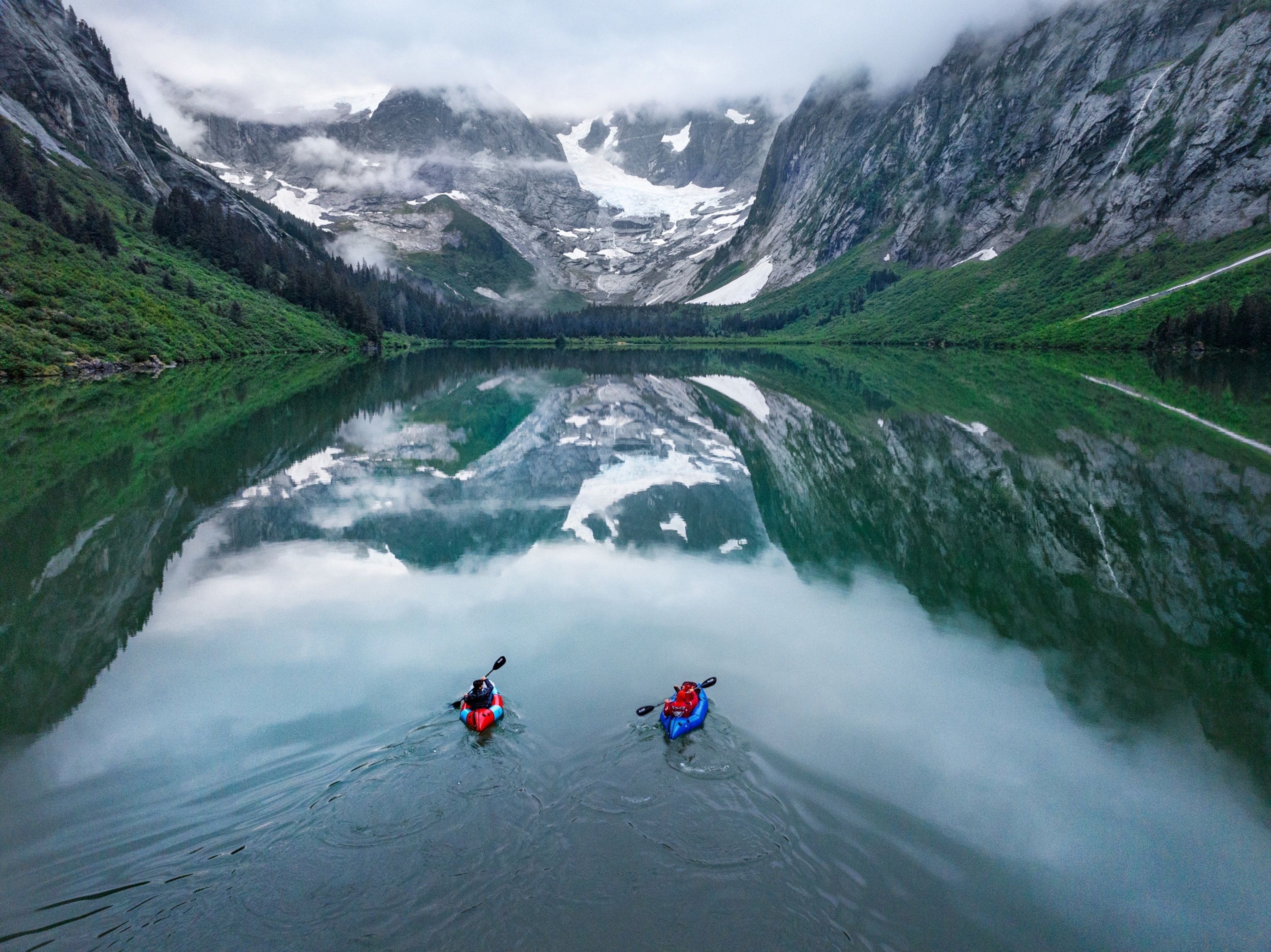 Honnold and Caldwell paddle in inflatable rafts. The snowy mountain tops reflect into the water.