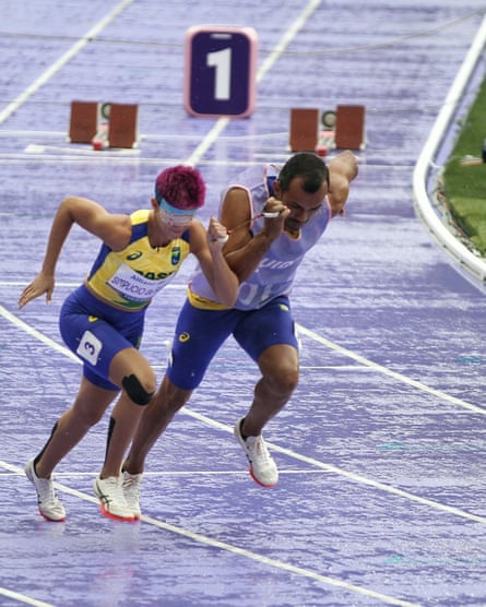 Thalita Vitória Simplicio da Silva runs with her eyes covered, accompanied by a sighted guide