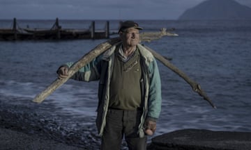 A man standing by the sea, holding large sticks over his shoulders