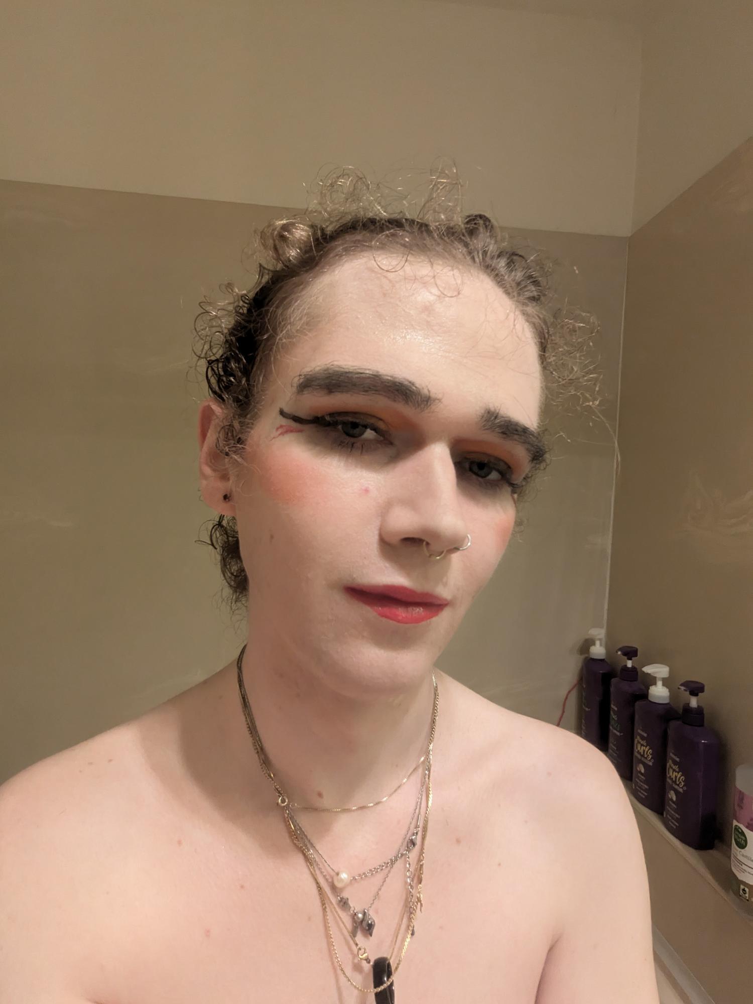 The photo shows a woman with curly hair tied back, wearing makeup...