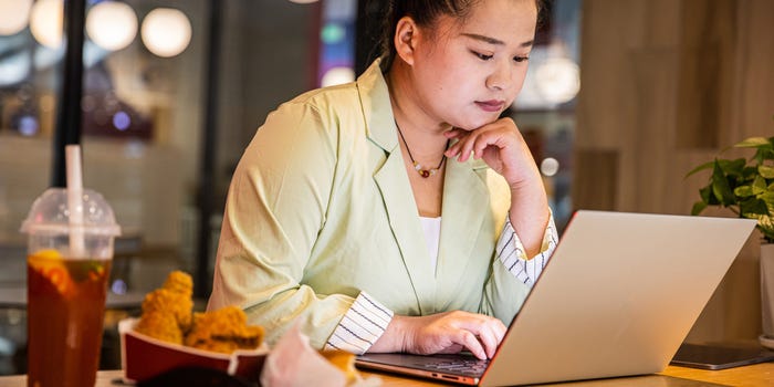 Serious young woman looks down at her laptop while sitting at a desk