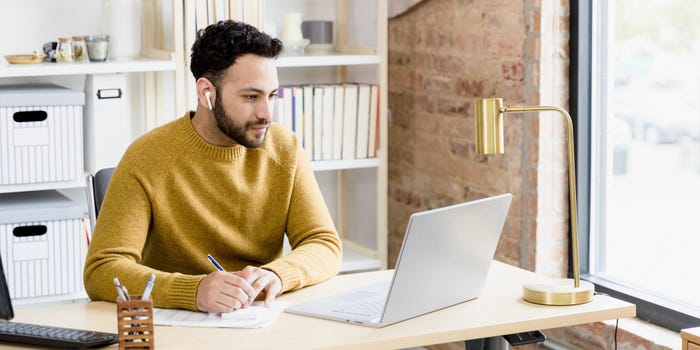 man writes on paper while doing research on computer at home