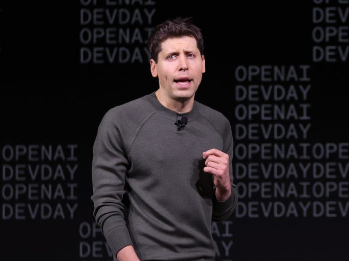 OpenAI CEO Sam Altman speaking in front of a black backdrop that says "OpenAI DevDay."