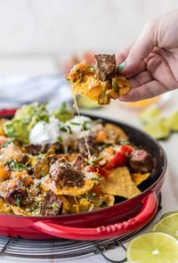 A skillet filled with nachos, topped with steak, cheese, peppers, and more