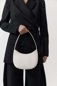 Shop the 90s Shoulder Bag in Cool White. The perfect companion for everyday wear to evening occasions. Subtle curved design with a zipper closure. Constructed from 100% lamb leather with goat suede leather lining. Made responsibly, designed in Byron Bay, Australia.