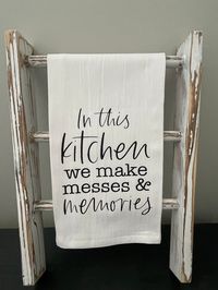 "In This Kitchen We Make Memories and Messes, Farmhouse Tea Towel, Kitchen Tea Towel Please note that these towels can be used to hang on an oven, hook, or mini ladder!  This towel measures 28\"x28\" Add this cute tea towel to your home décor or give as a gift! Mini Ladders are not included in this purchase. CARE INSTRUCTIONS: Wash on cold, gentle cycle. Dry on low heat."