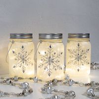 Brighten up your indoor holiday décor with this set of three mason jars filled with delicate fairy string lights. Each frosted jar features a silver glitter and gem snowflake on the front and back. To turn on the warm white fairy lights, simply unscrew the mason jar lid and turn the lights on with the switch. There is a convenient timer option on the switch for 6 hours on and 18 hours off. These beautiful mason jars will add lovely illumination to a mantel, table setting, or centerpiece. Each ma