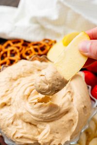 Glass bowl with creamy peanut butter dip served with apple slices, strawberries and pretzels.