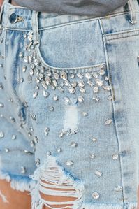 We don't think we could have found a more Glitzy Bella pair of denim cut offs! The crystals are stunning and the workmanship is incredible. Throw these shorts on with a basic white tee or your favorite bodysuit and your outfit is done! These shorts feature a mid rise waist with a classic button zipper closure, functional pockets at the waist, light distressing, and the most fabulous rhinestone stud detailing! Fit: These shorts are high-waisted and intended to be fitted at the waist and slightly