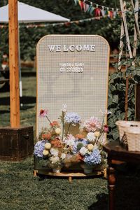 charming rattan wedding welcome sign with pastel primary color floral arrangements for a sunny outdoor ceremony