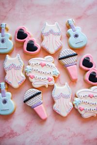 Royal icing decorated Taylor Swift Eras Tour Lover cookies. Designs include a friendship bracelet cookie that says “In My Lover Era”, a microphone cookie, a heart sunglasses cookie, a guitar cookie, and a Lover bodysuit cookie. All made in a pink, blue, and purple theme with edible glitter. Cookies were made for movie night party for Taylor Swift: The Eras Tour Movie. The cookies are to reflect her first era in the concert being Lover.