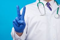 male hand in blue sterile medical gloves shows victory gesture, concept of victory over the disease, positive emotions