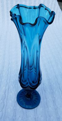 "This is a Viking Glass swung vase made in the 60's-70's.  It's an interesting color- between a peacock blue and a midnight or \"Montana\" blue, to borrow from the Swarovski crystal color.  It's in great condition; there are just a couple tiny little rough patches along the edge of the \"swag\" part- the bulbous part of the vase where there's a sort of gathered valance-type design.  You can also see in the picture, there is a trapped bubble in the glass near the rim.   None of these characterist