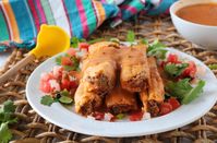 A plate of tamales smothered in sauce with a bowl of tamale sauce in the background.