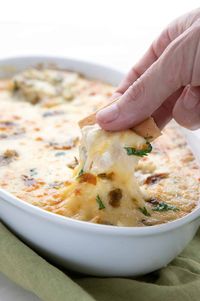 A hand digging a cracker into Green Chili Dip.