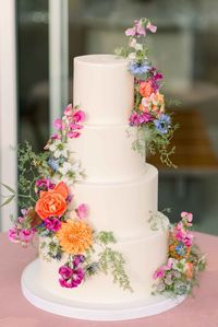 The tiered wedding cake with flowers in bright blue, coral, pink and orange with delicate greenery.