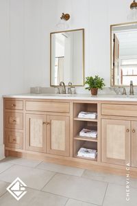 This cottage full bath features hints of a boho-style aesthetic. The custom vanity is crafted with rift white oak and has a framed inset caned with rattan material. The earthy tones and bright accents bring a warm and neutral feel to this space, and of course, we love how the bronze hardware ties everything together. #ChervinKitchen #CustomCabinetry #FullBath #BohoStyleBathroom #RattanMaterial #EarthyTonedBathroom