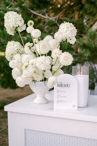 If you are planning at all white party, save this photo as decor inspiration for your event! This bar featured a white acrylic bar menu sign and elegant white floral arrangement. This is the perfect decor for a white wedding of all white party!