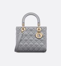 The Lady Dior bag epitomizes the House's vision of elegance and beauty. Refined and sleek, this creation is timeless. Crafted in opaline gray pearlescent lambskin with Cannage stitching, it features an instantly recognizable quilted texture. The pale gold-finish metal D.I.O.R. charms embellish and illuminate its silhouette. Equipped with a thin, removable leather shoulder strap, the medium Lady Dior bag can be carried by hand or worn crossbody..