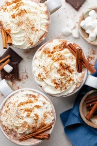 Three mugs with hot chocolate and whipped cream on top.