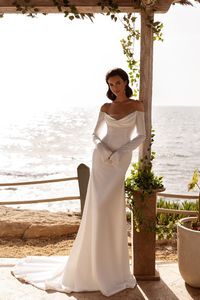 This silk/satin long-sleeved off-the-shoulder wedding gown exudes elegance with its cowl neck design. Bordering the gown with sparkling jewels adds a luxurious and glamorous look for a bride seeking a sophisticated and dazzling ensemble.