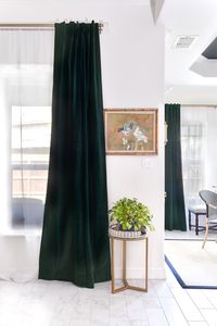 Dark emerald green velvet curtains hanging in an open concept living and dining room area with black tray ceilings and white walls.