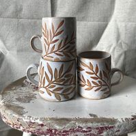 Wax relief mug. Hand thrown on the potters wheel using stoneware clay, I've then hand painted the leaf design using wax, before dipping in white glaze and firing. The areas painted in wax 'resist' the glaze and once fired the ceramic body is left exposed, creating the design. Due to their handmade nature they may vary slightly from the one pictured.  All pieces come packaged in plastic free packaging to ensure they reach you in perfect condition.