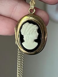 Embrace the timeless beauty of vintage fashion with this exquisite Cameo Locket Necklace, a piece of costume jewelry that captures the elegance and charm of a bygone era. This stunning necklace features a classic cameo pendant, showcasing the traditional profile of a delicate figure in relief, set against a contrasting background that highlights its intricate details. Cameos have been treasured for centuries as symbols of refinement and sophistication. They often depict portraits, mythological s