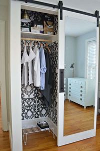 Small closet with sliding, mirrored barn door and bold black and white damask wallpaper within. If you've been scared to try wallpaper, a closet is a great place to give it a go!