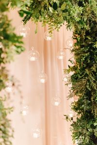 Need wedding decor inspiration? How about these hanging candles in glass bubbles as a ceremony backdrop. We framed the arch with green garland and added LED candles to make sure it was safe!  #ceremonyideas #hangingcandles #floatingcandles