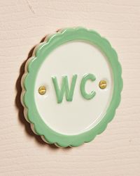 In a shiny green glaze and circular profile, this ceramic WC sign has a scalloped edge.