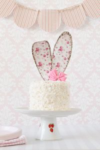 An easy and adorable coconut cake for Easter, decorated with floral paper bunny ears, and a pink candy melts bow.