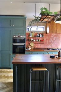 Kitchen with large wooden island with green cabinets and terracotta backsplash.