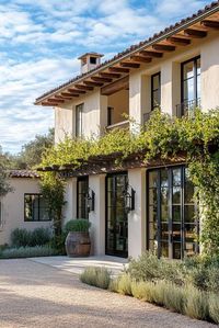 Modern Italian mediterranean house facade with vine covered pergola olive tree lined front yard. Check out all of these stunning Italian Mediterranean houses that encapsulate elegant arches, textured stucco, charming terra cotta details, and so much more.